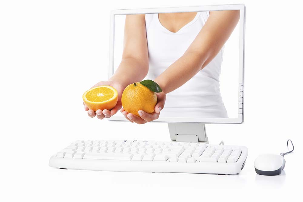 Female hand holding orange coming out from computer screen